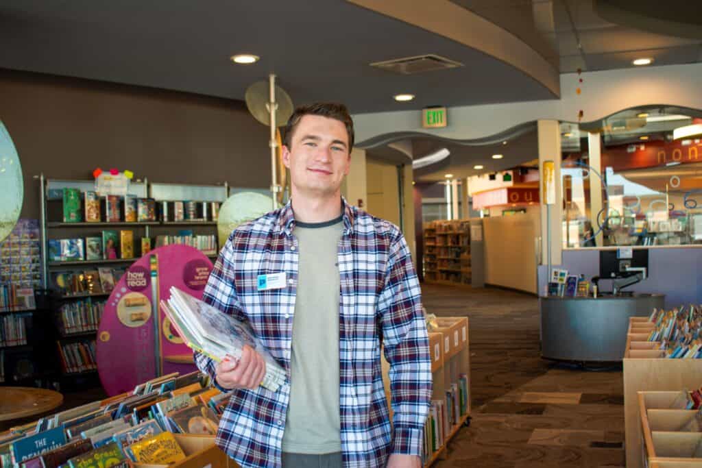 Benjamin Brantley, library staff, smiling and holding a book inside Council Tree Library